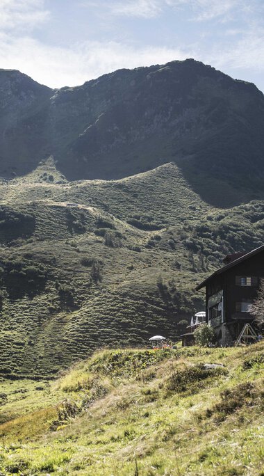 Ein Haus in den grünen Hügeln des Schwarzwassertals, umgeben von Bergen bei schönem Wetter. | © Kleinwalsertal Tourismus eGen • Fotograf: Andre Tappe
