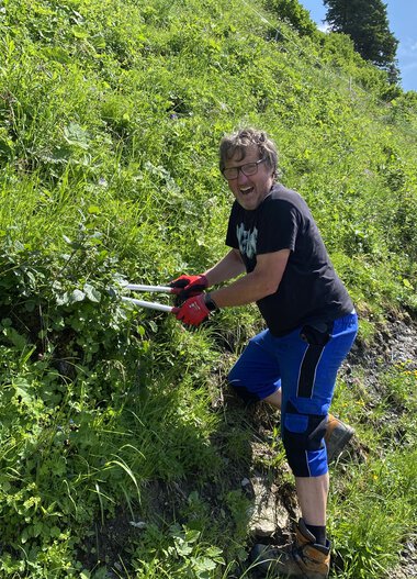 Junge Frau beim Schneiden von Zweigen im Grünen an einer steilen Wegböschung während einer Freiwilligenaktion im Juli 2021. | © Kleinwalsertal Tourismus eGen